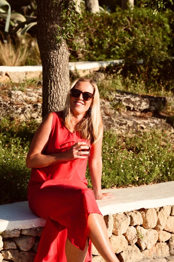 casey wearing a red dress sitting outside in the sun on a bench