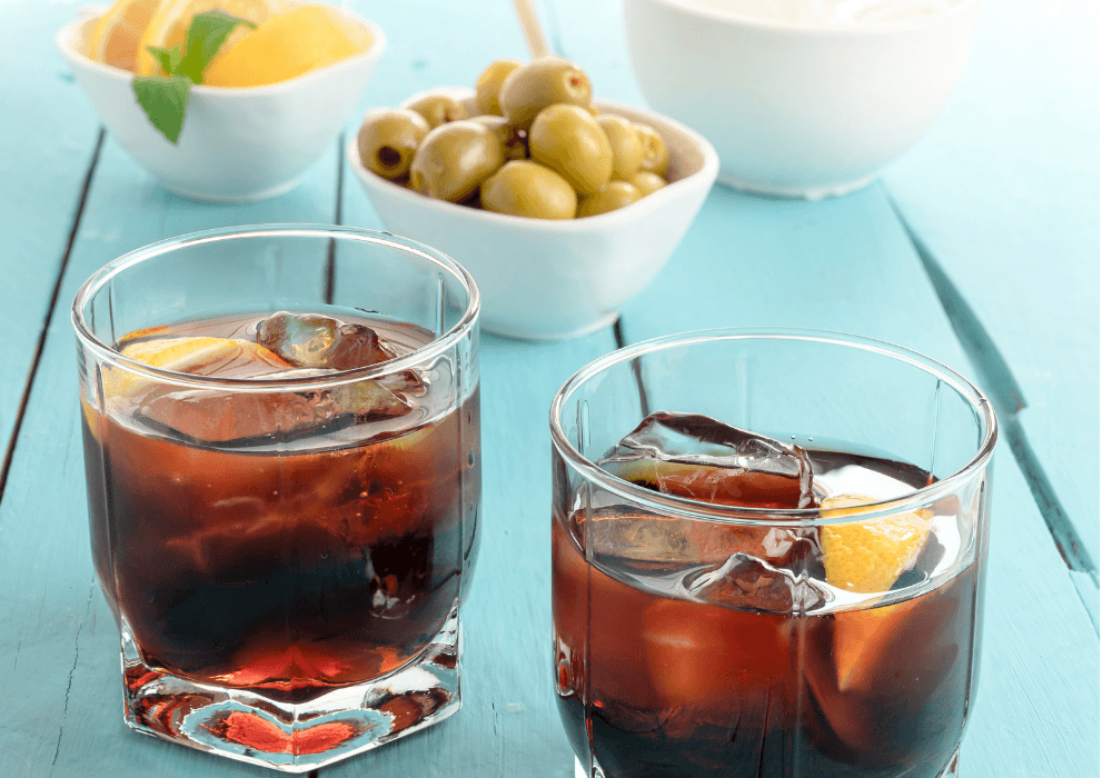 2 glasses of vermouth on a blue table with olives