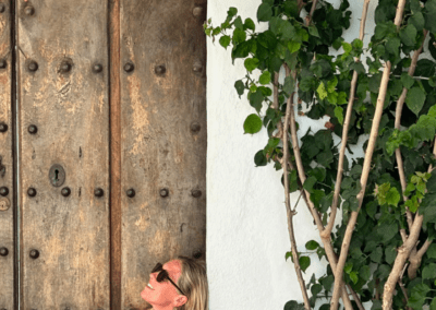 casey from biznaga sitting in front of a rustic door in a pink dress