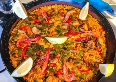 spainish paella sitting on a table with lemon wedges