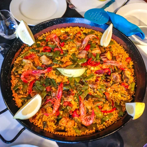 spainish paella sitting on a table with lemon wedges